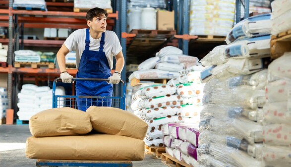 Lagerarbeiter schiebt einen Wagen mit S&auml;cken durch ein Warenlager
