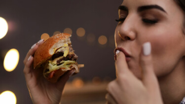 Junge Frau mit einem Burger in der Hand schleckt sich den Zeigefinger ab.