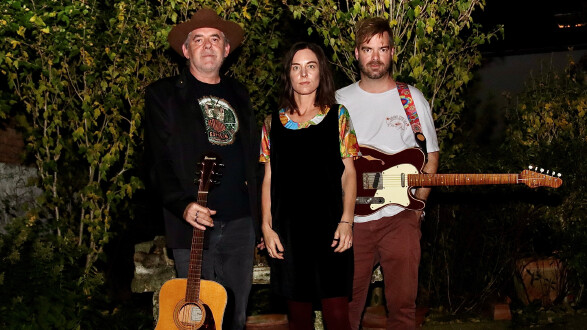 Drei Personen stehen draußen vor dichter Gartenvegetation. 