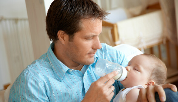 Vater f&uuml;ttert sein Baby mit einer Milchflasche im Wohnzimmer.