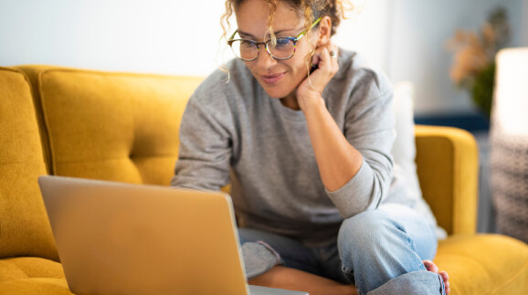 Eine Frau sitzt auf einem Sofa und nutzt ein Ger&auml;t zum Online-Shopping.