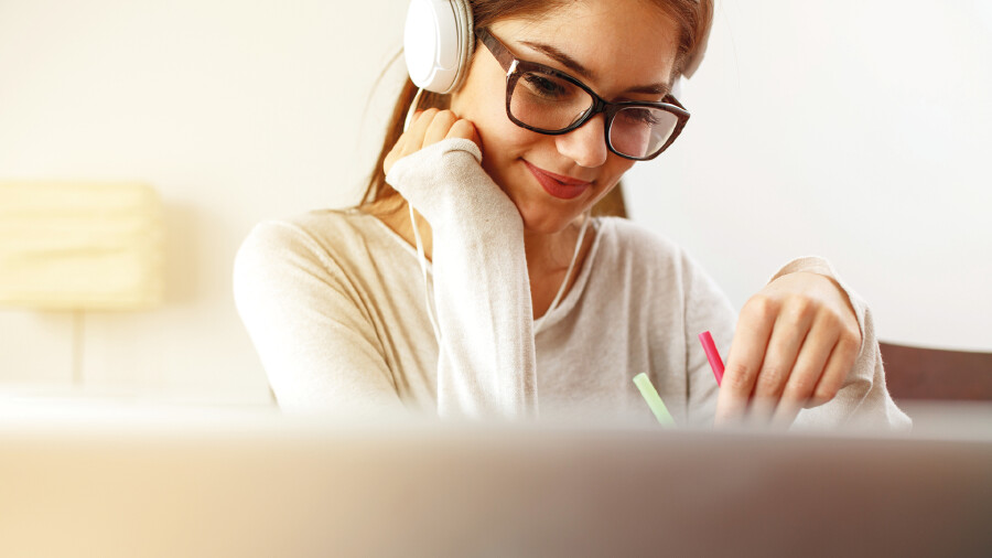 Person mit Kopfh&ouml;rern und Brille sitzt beim Schreibtisch