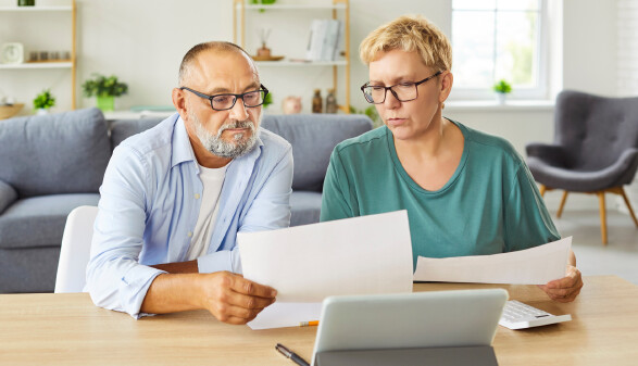 &Auml;lteres Paar sitzt mit Tablet und Unterlagen am Tisch und bespricht seine Finanzen.