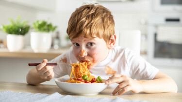 Ein kleiner Junge isst Spaghetti Bolognese.