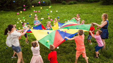 Kinder und Betreuerinnen stehen im Kreis auf einer Wiese