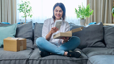 Junge Frau packt ein Paket mit einem neuen Smartphone aus, das sie online bestellt hat.