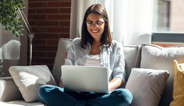 Frau sitzt auf einem Sofa und nutzt einen Laptop.
