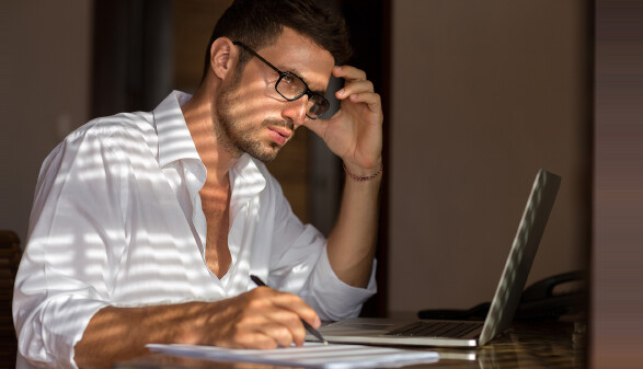 Mann mit Brille sitzt bei Notebook und überlegt