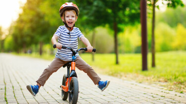 Lachendes Kind mit Helm f&auml;hrt mit dem Laufrad durch den Park