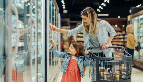 Frau und Kind mit Einkaufswagen vor dem Tiefk&uuml;hlregal im Supermarkt,