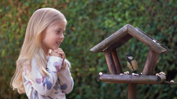 Kleines M&auml;dchen steht vor Vogelhaus