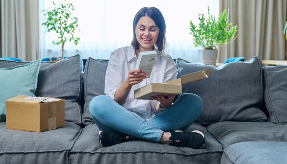 Junge Frau packt ein Paket mit einem neuen Smartphone aus, das sie online bestellt hat.