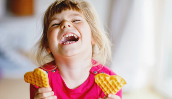 Ein lachendes M&auml;dchen mit je einem Keks in der Hand.