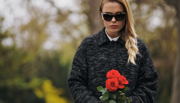 Junge Frau mit Sonnenbrille und roten Rosen am Friedhof