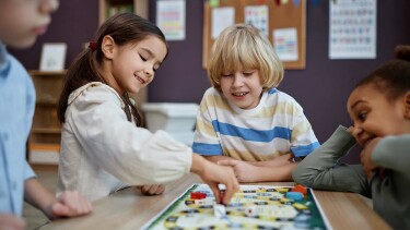 Vier Kinder sitzen um einen Tisch und spielen gemeinsam ein Brettspiel.