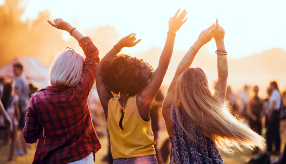 Drei junge Menschen, von hinten zu sehen, feiern tanzend auf einem Festival.