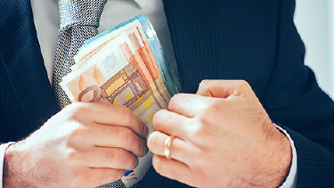 Mann in Anzug steckt Geldscheine in die Innentasche des Sakkos