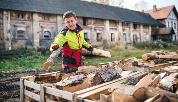 Ein junger Mann schlichtet Brennholz in Kisten.