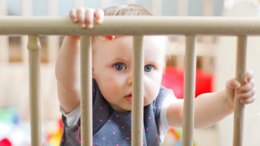 Baby hält sich mit beiden Händen an einem Treppenschutz fest und schaut neugierig hindurch.