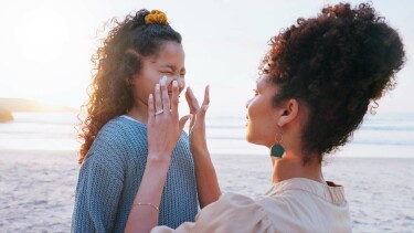 Eine Mutter cremt ihrer Tochter am Strand das Gesicht mit Sonnencreme ein.