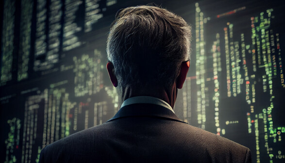 Gesch&auml;ftsmann an der B&ouml;rse blickt auf Aktienkurse an der Wand.