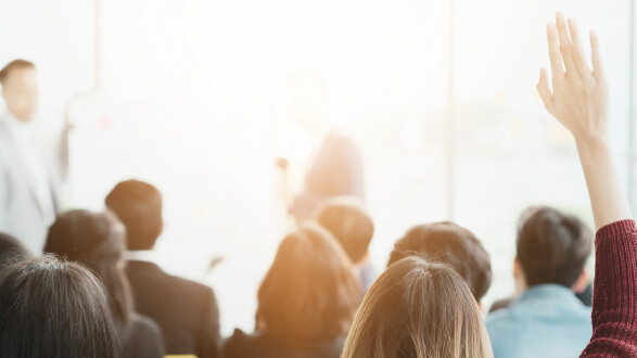 Mehrere Menschen sitzen in einem hellen Konferenz- oder Schulungsraum und hören einer Vortragsperson zu. Im Vordergrund hebt eine Person die Hand, um sich zu melden. Das Licht ist warm und freundlich, die Stimmung wirkt konzentriert und interessiert. © Me studio, stock.adobe.com Personen sitzen in einem Seminarraum, eine Person hebt die Hand, um eine Frage zu stellen.