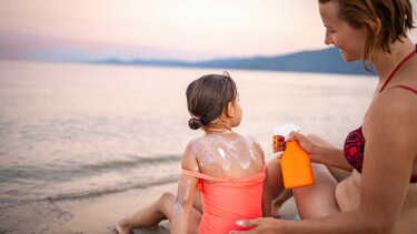Eine Frau trägt einem Kind am Strand Sonnencreme auf den Rücken auf.