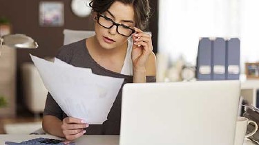 Frau mit Brille sitz vor Ihrem Laptop und prüft Unterlagen © Fotolia.com, gpointstudio