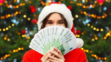 Frau mit Weihnachtsm&uuml;tze h&auml;lt Geldscheine vor ihr Gesicht. &copy; Syda Productions, Adobe Stock