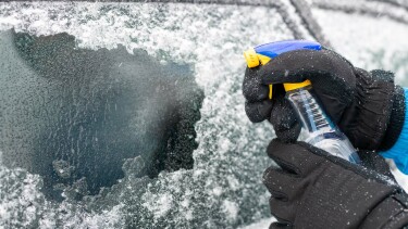 Person spr&uuml;ht Enteiser auf eine vereiste Autoscheibe.