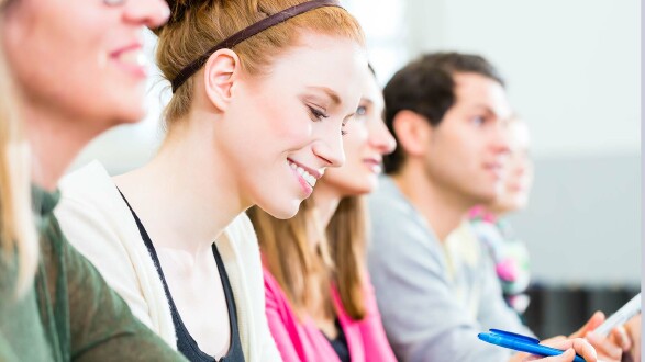 5 junge, gl&uuml;ckliche Menschen sitzen in einer Reihe und machen sich Notizen.