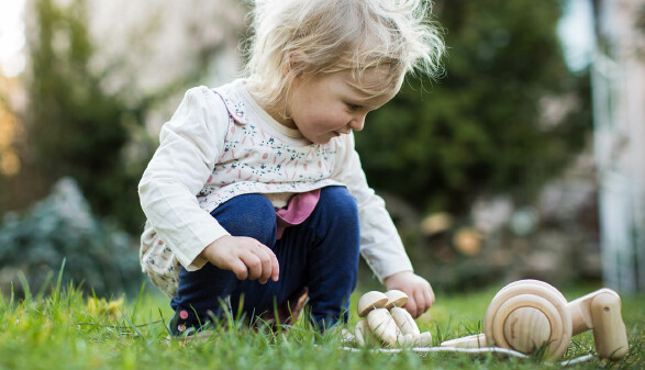 Kleinkind spielt im Garten mit Holzspielzeug