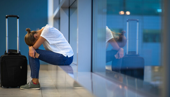 Ersch&ouml;pfte junge Frau wartet mit ihrem Trolley am Flughafen auf ihren versp&auml;teten Flug.