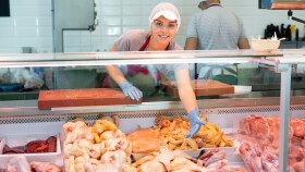 Eine Verk&auml;uferin steht hinter einer Vitrine mit Fleisch und pr&auml;sentiert die Produkte.