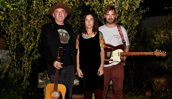 Drei Personen stehen drau&szlig;en vor dichter Gartenvegetation. 