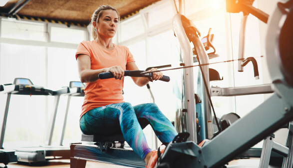 Frau trainiert auf einem Rudergerät im Fitnessstudio, konzentriert beim Ganzkörpertraining in heller, moderner Umgebung.