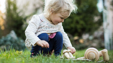 Kleinkind spielt im Garten mit Holzspielzeug