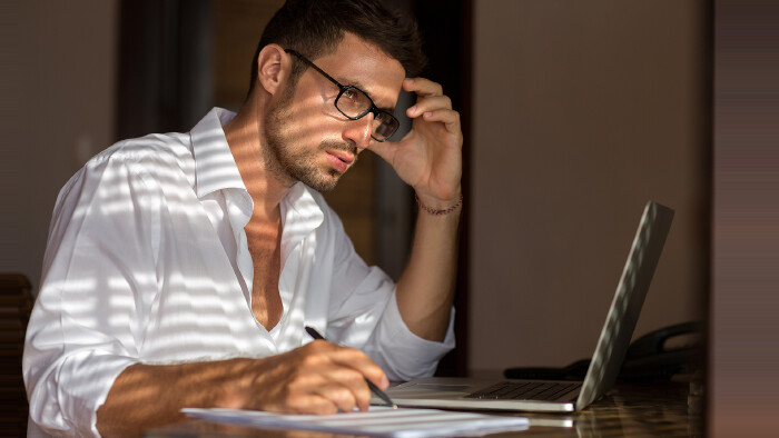 Mann mit Brille sitzt bei Notebook und überlegt