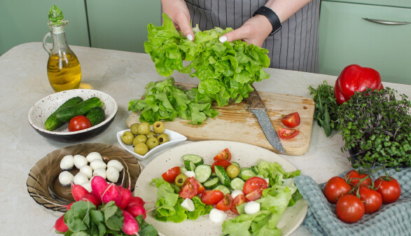 Eine Person bereitet Salat aus Tomaten, Gurken, Oliven und Mozzarella zu.