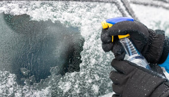 Person spr&uuml;ht Enteiser auf eine vereiste Autoscheibe.