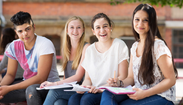 Vier Sch&uuml;ler:innen sitzen am Schulhof und lernen