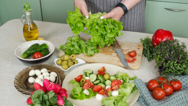 Eine Person bereitet Salat aus Tomaten, Gurken, Oliven und Mozzarella zu.