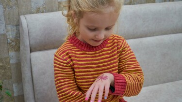 Ein kleines M&auml;dchen betrachtet das Klebetattoo auf ihrem Handr&uuml;cken.