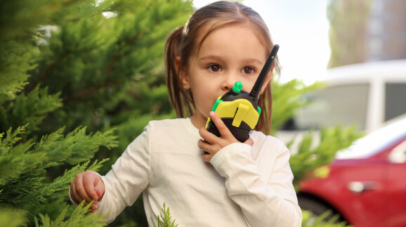 Ein Kind mit einem Walkie-Talkie hinter einem Baum.