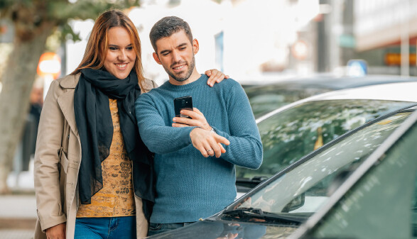 Junges Paar mit Smartphobe schaut sich Gebrauchtwagen an.