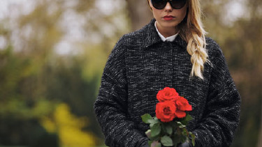 Junge Frau mit Sonnenbrille und roten Rosen am Friedhof