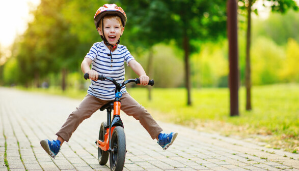 Lachendes Kind mit Helm f&auml;hrt mit dem Laufrad durch den Park