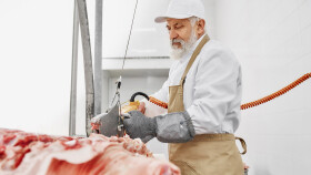 &Auml;lterer Metzger mit wei&szlig;em Bart und wei&szlig;em Kapperl zerschneidet maschinell ein Schwein.