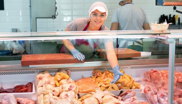 Eine Verk&auml;uferin steht hinter einer Vitrine mit Fleisch und pr&auml;sentiert die Produkte.