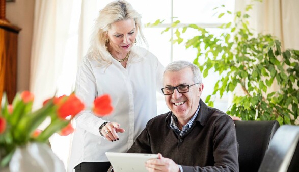 Zwei &auml;ltere Menschen an einem Tisch, er schaut vom Notebook auf, sie sieht ihn an. 